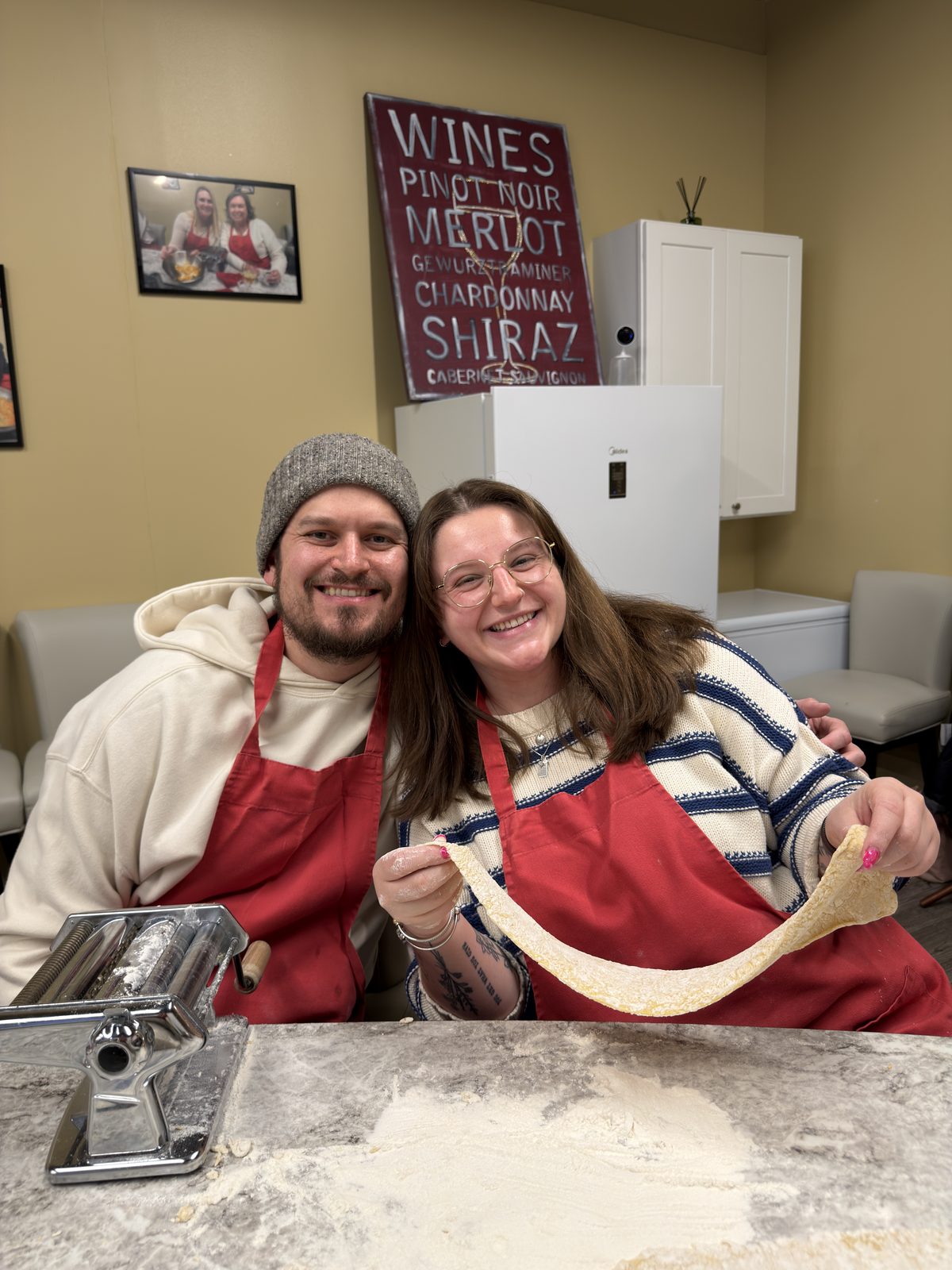 Cody and Laura making fresh pasta in matching red aprons